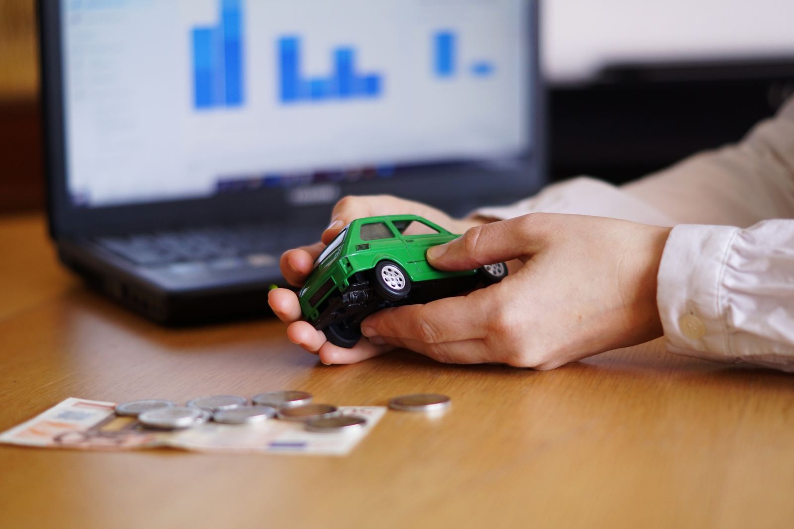 Pessoa segurando uma miniatura de carro ao lado de moedas e notas de dinheiro, representando a franquia do seguro auto